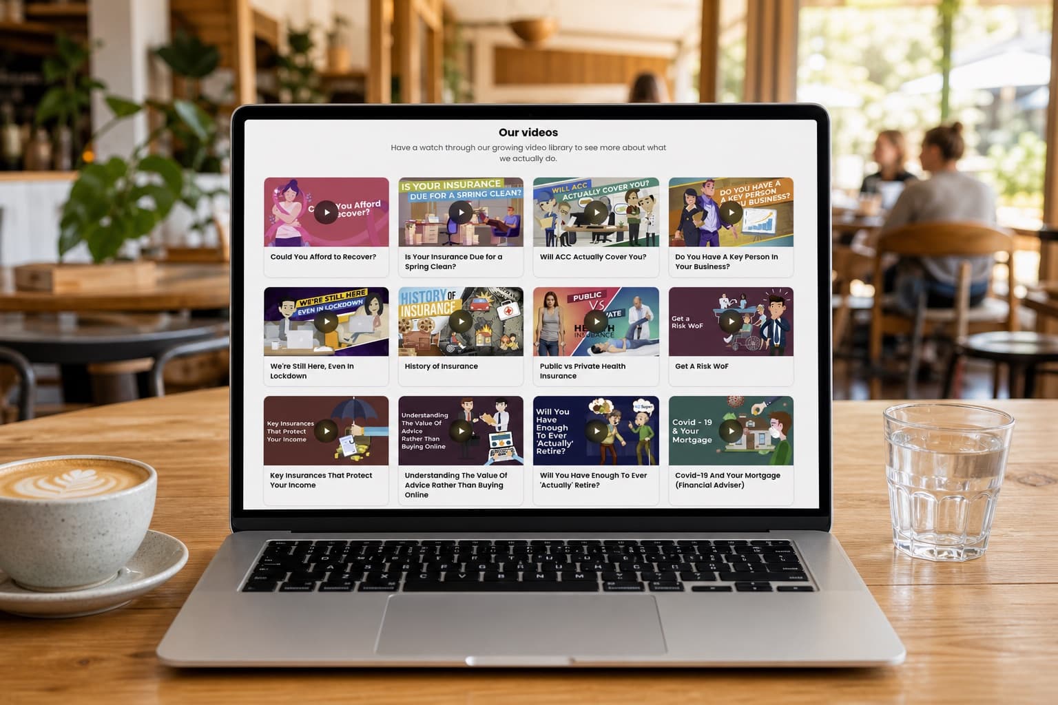 A laptop on a cafe table showing an adviser's website with a wall of their video library embedded in it